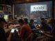 People using betting apps on smartphones inside a bar as a Kalshi billboard is installed outside in the rain, symbolizing the platform’s Brazil launch amid a national gambling addiction crisis